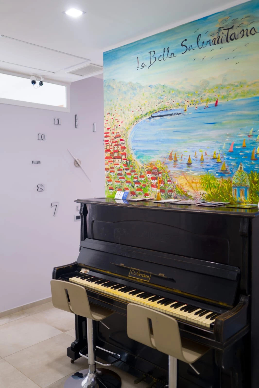 Pianoforte nero in una sala, parete bianca con numeri e grande murale marino colorato.