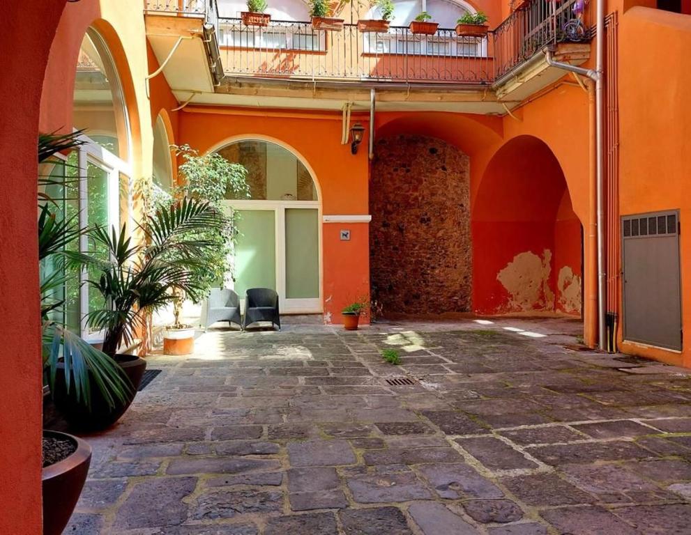 Cortile interno con pavimento in pietra, archi colorati, piante in vaso e sedie vicino a una porta.