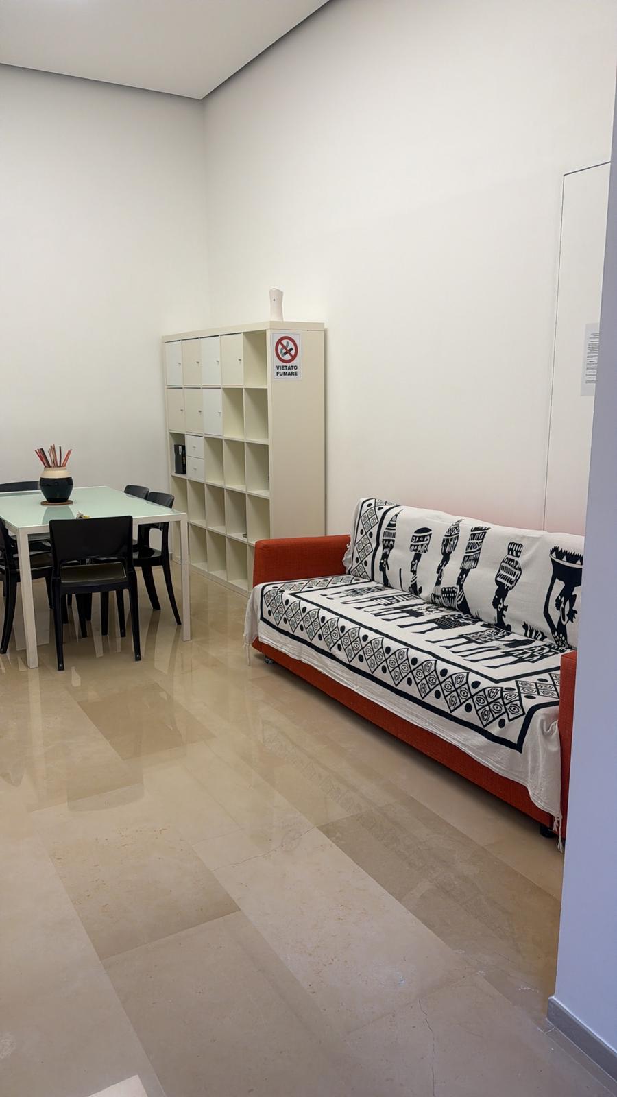 Soggiorno moderno con divano letto, tavolo, sedie e scaffale bianco con divieto di fumare.